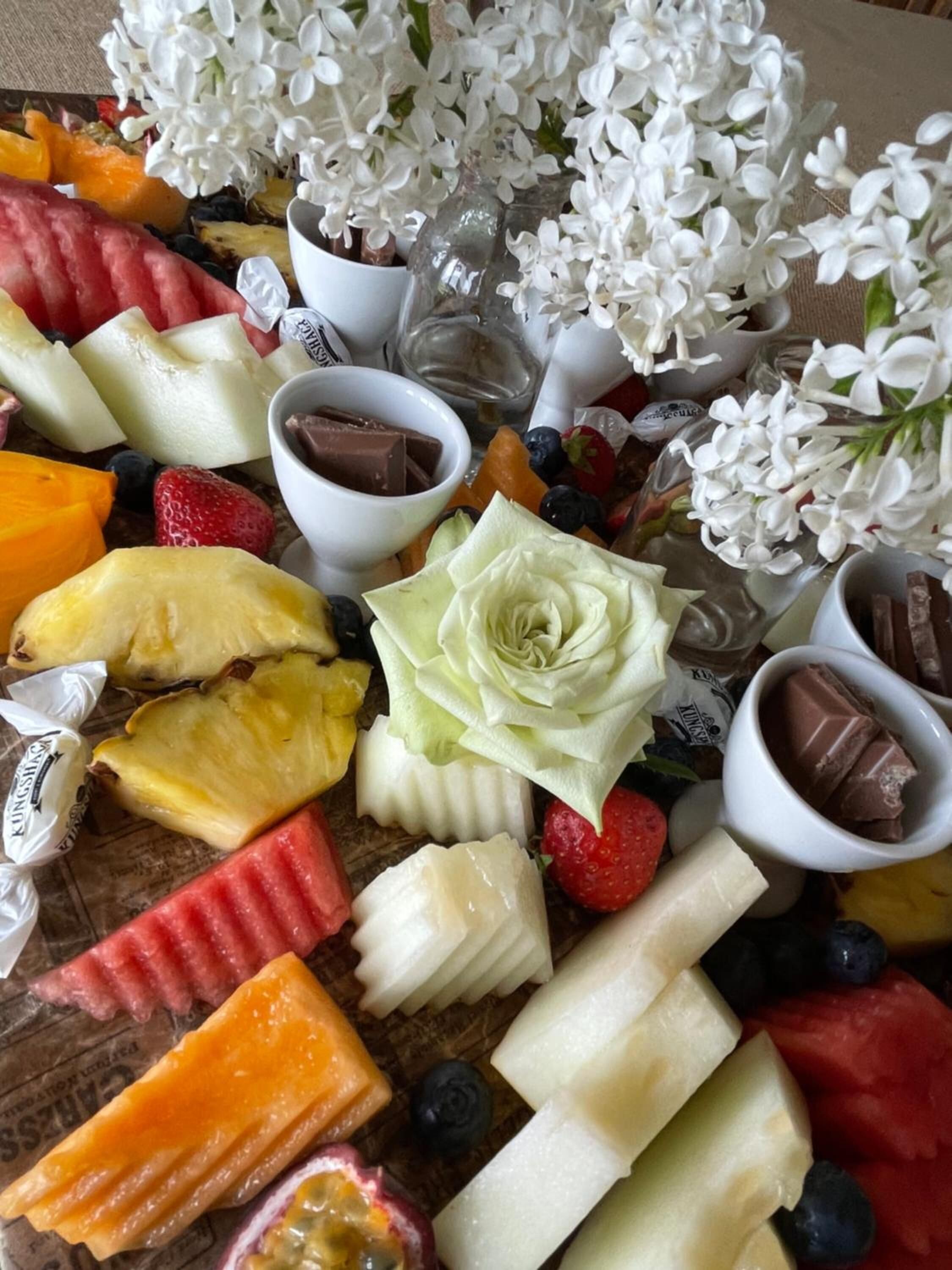 Een fruitschaal met verschillende soorten fruit, chocolade en een decoratieve witte bloem.