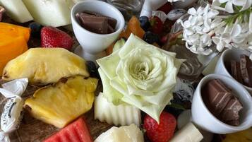 Een fruitschaal met verschillende soorten fruit, chocolade en een decoratieve witte bloem.