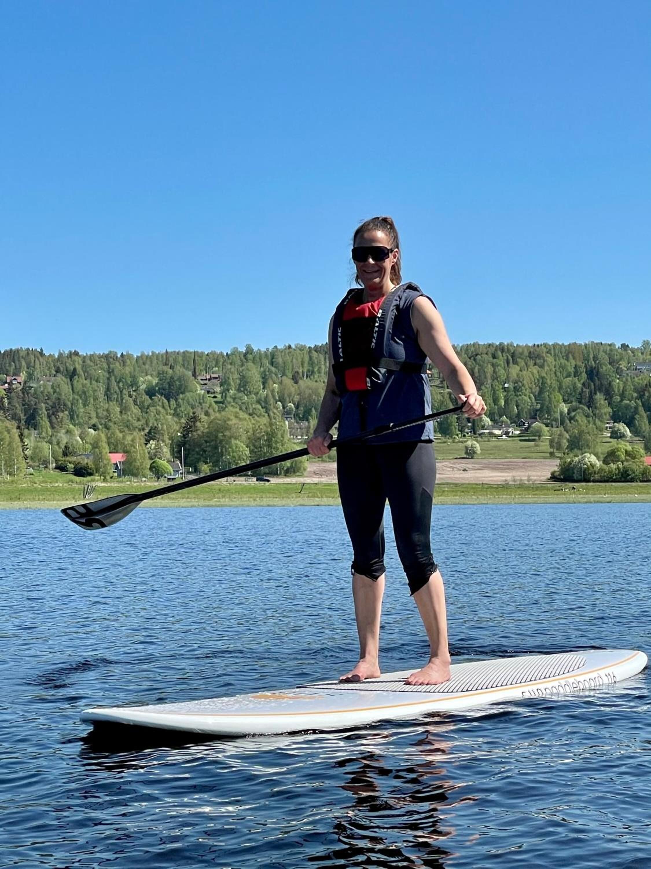 A person paddleboarding on a calm lake with a forested shoreline in the background.
