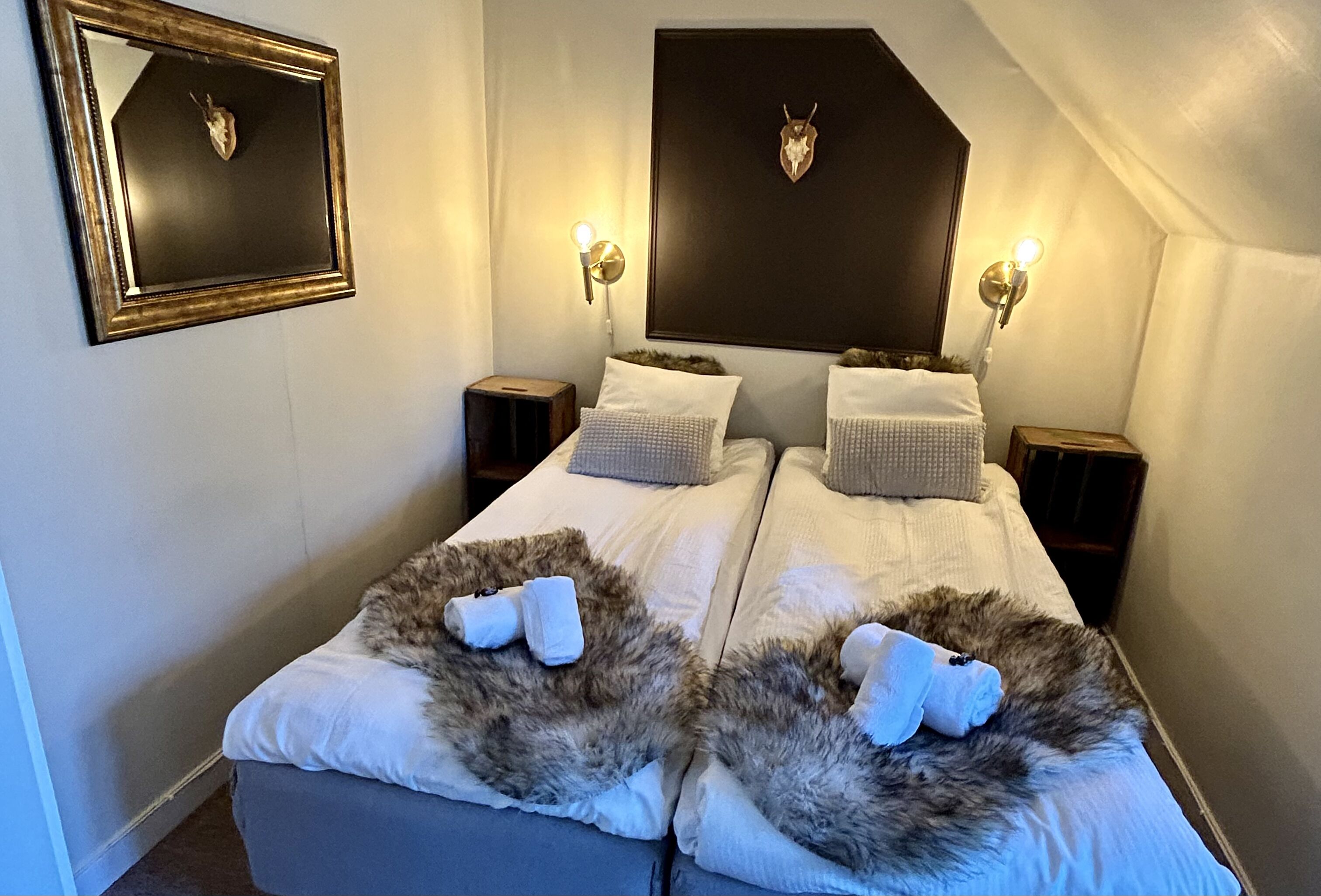 Ein Doppelbett mit weißer Bettwäsche und zwei flauschigen Kissen, ein aufgehängter Hirschkopf an der Wand und zwei Wandleuchten.