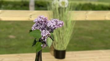 A table with a meal, a drink, and a flower arrangement on a deck with a view of a field and mountains.