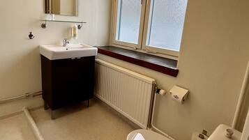 A small bathroom with a white sink, dark cabinet, window, radiator, and toilet.