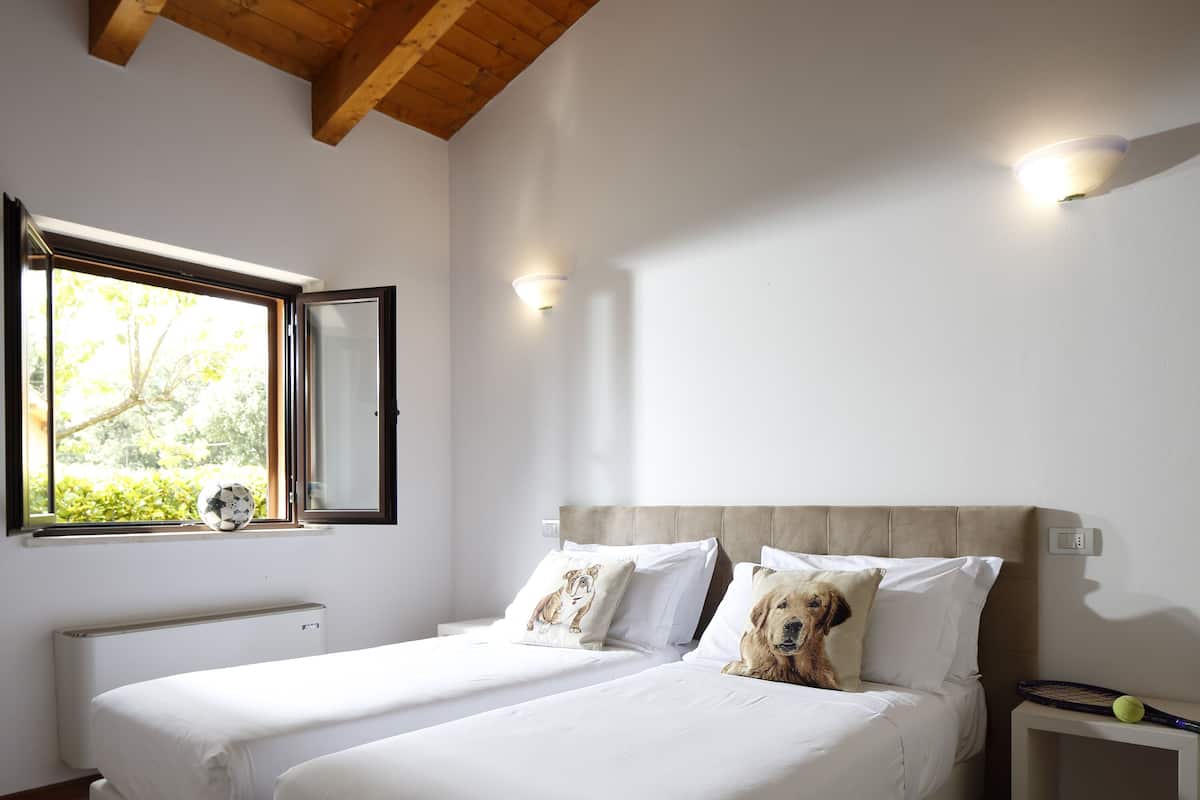 A bedroom with two beds, a window with a view, and a wall-mounted light fixture.