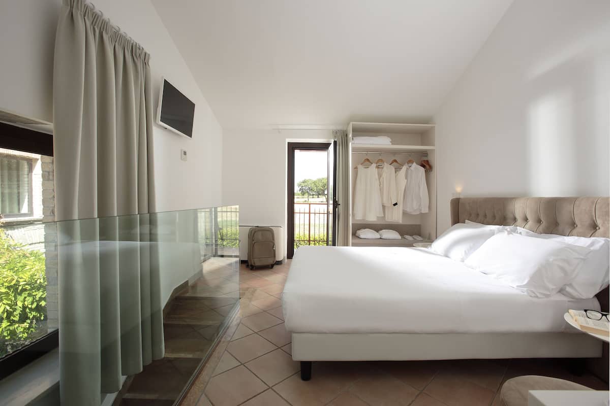 A hotel room with a bed, a wardrobe, a suitcase, and a balcony with curtains.