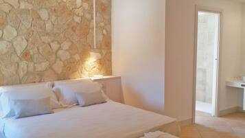 A bedroom with a stone wall, a bed with white linens, and a bathroom visible through an open door.