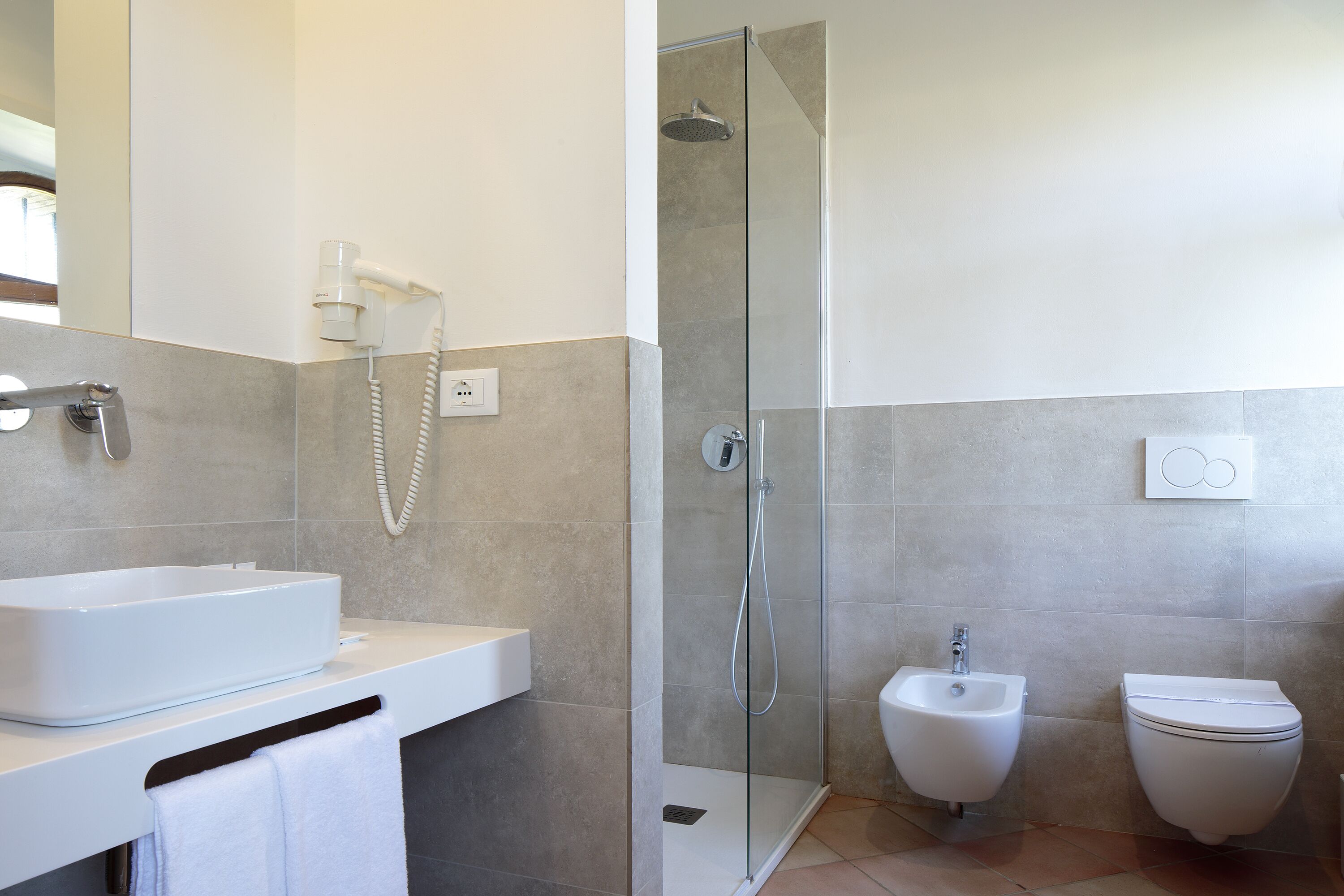 A modern bathroom with a glass-enclosed shower, a bidet, and a white sink.