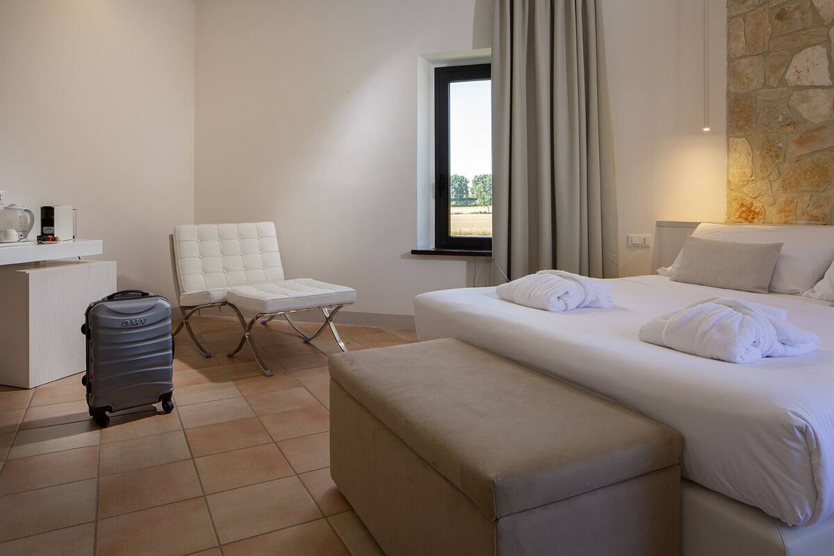 A hotel room with a bed, a chair, a desk, and a suitcase.