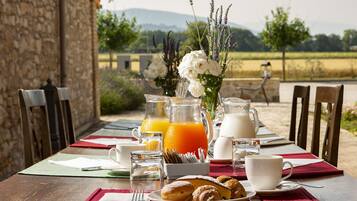 A breakfast table set outdoors with a view of a field and mountains.