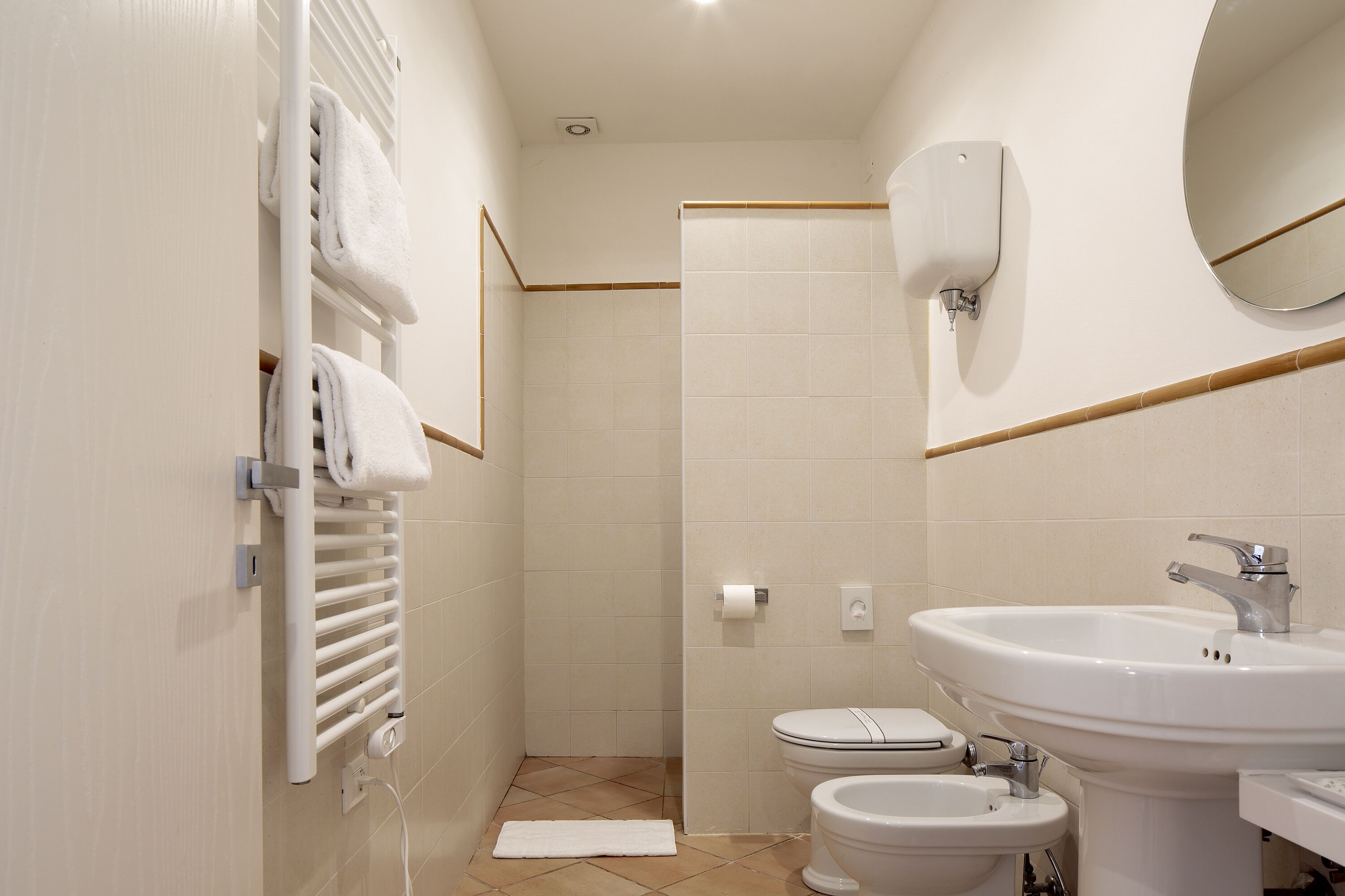 A modern bathroom with a toilet, bidet, sink, towel rack, and a mirror.