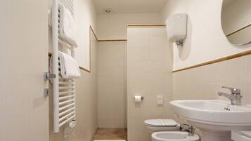 Une salle de bain moderne équipée d’un WC, d’un bidet, d’un lavabo, d’un porte-serviettes et d’un miroir.