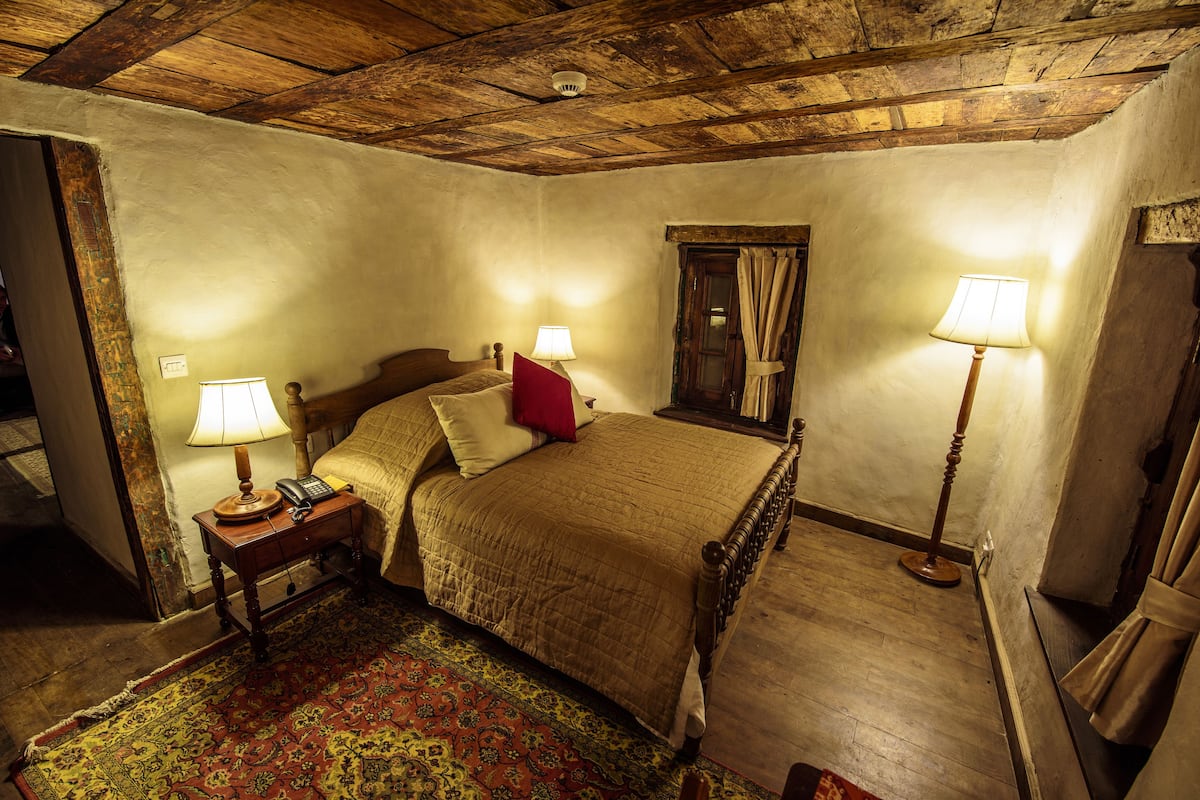 Une chambre de style traditionnel avec un plafond en bois, un lit agrémenté d’un oreiller rouge, deux lampes de chevet et un tapis à motifs.