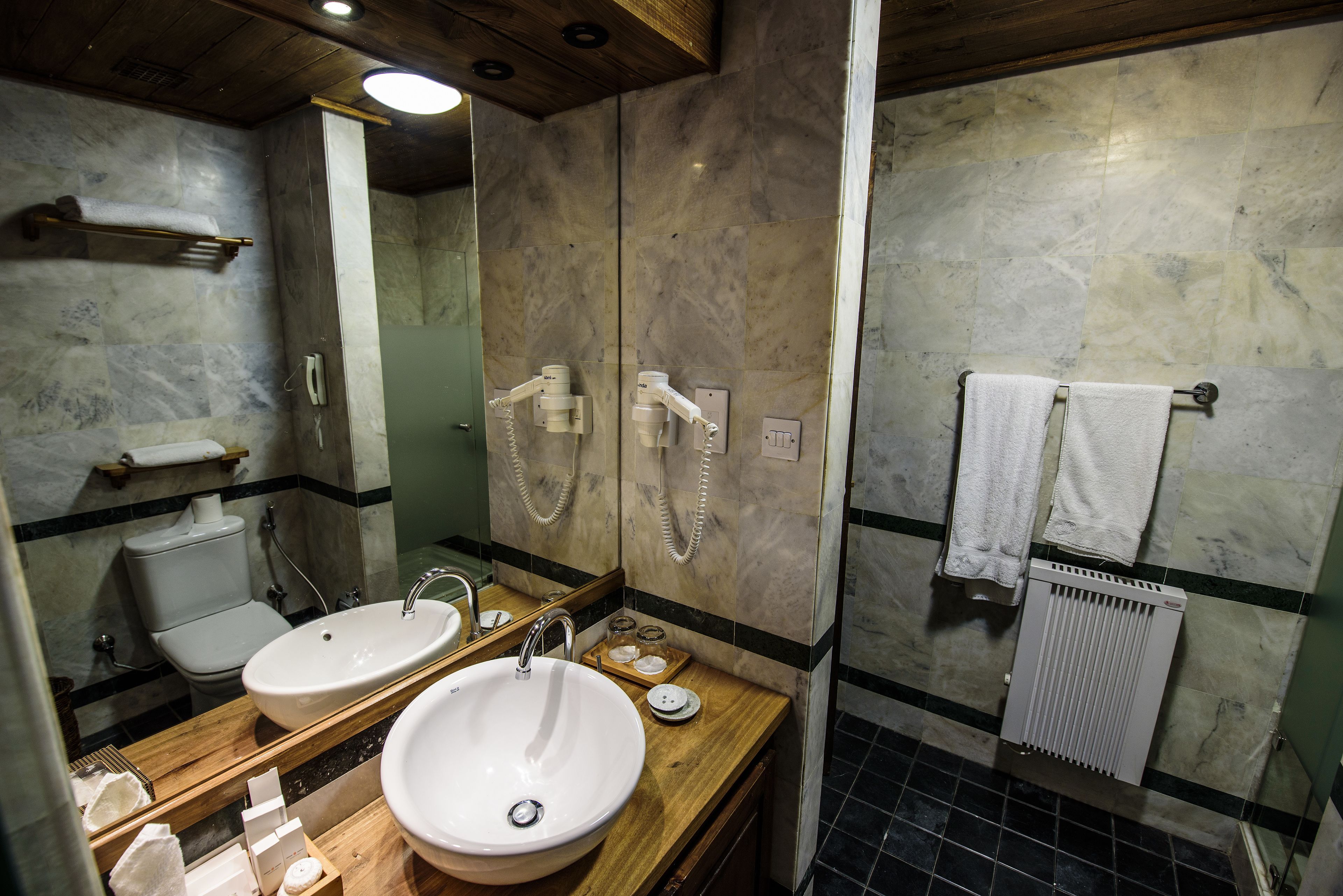 A bathroom with a wooden vanity, two sinks, a toilet, and a mirror.