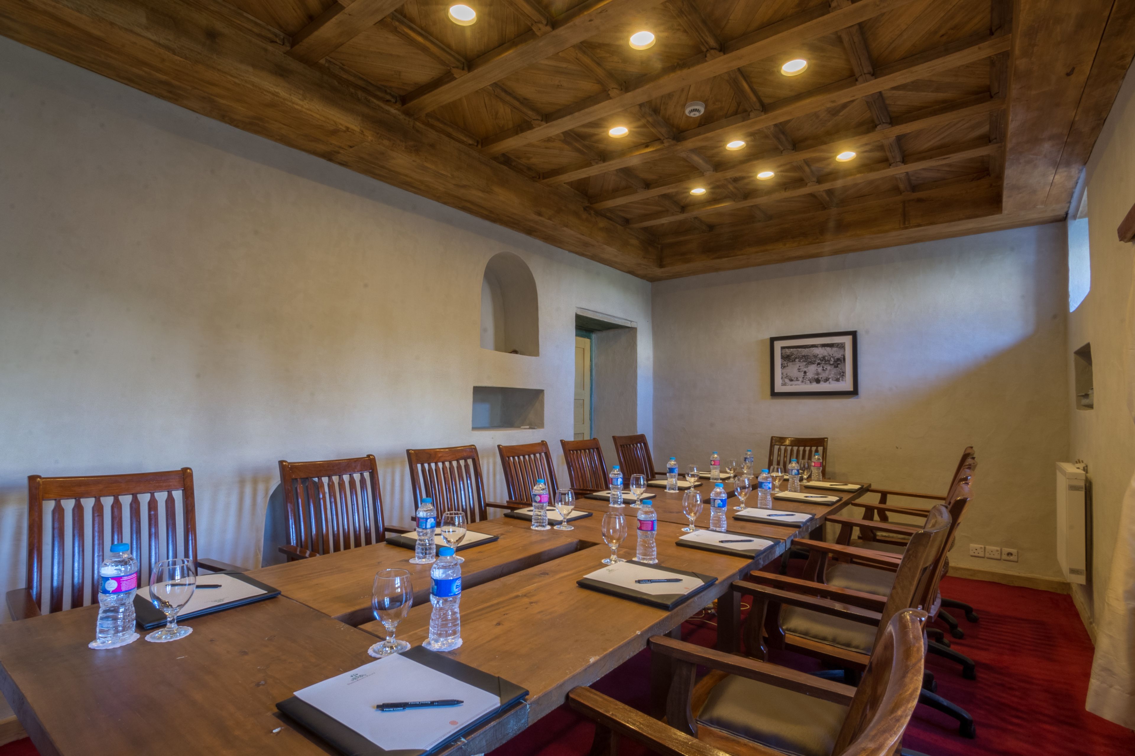 A conference room with a long wooden table, multiple chairs, water bottles, glasses, and a framed picture on the wall.