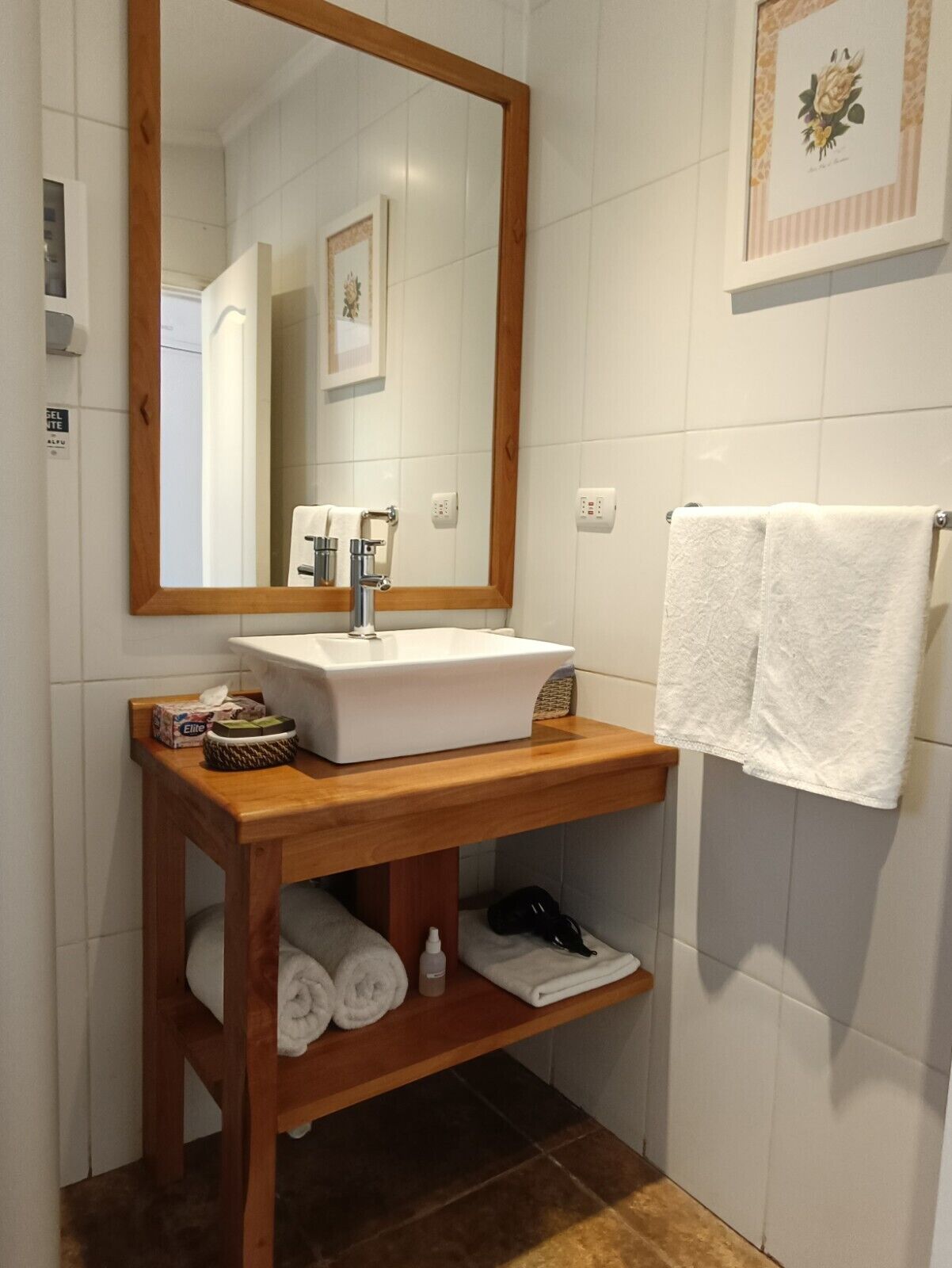 A bathroom with a wooden vanity, white sink, and a large mirror. There are towels and toiletries on the vanity.