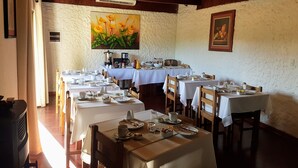 Un espace repas avec plusieurs tables préparées pour le petit-déjeuner, comprenant des nappes blanches, des chaises en bois et divers éléments pour le petit-déjeuner.