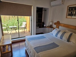 Un dormitorio con cama, una mesita, una silla, cabecera de madera, una mesita de noche y vistas a un jardín a través de una puerta corrediza.