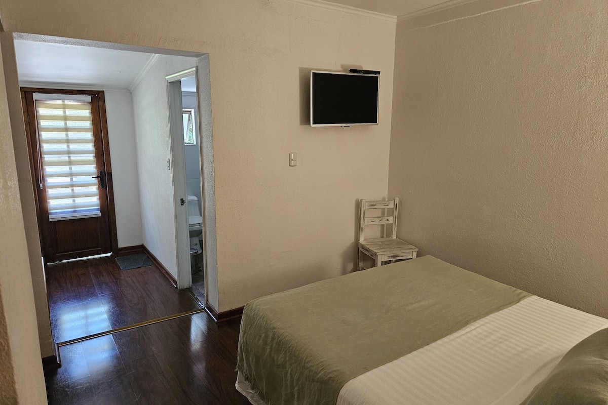 Une chambre à coucher avec un lit, un téléviseur fixé au mur et une porte donnant sur une salle de bain.
