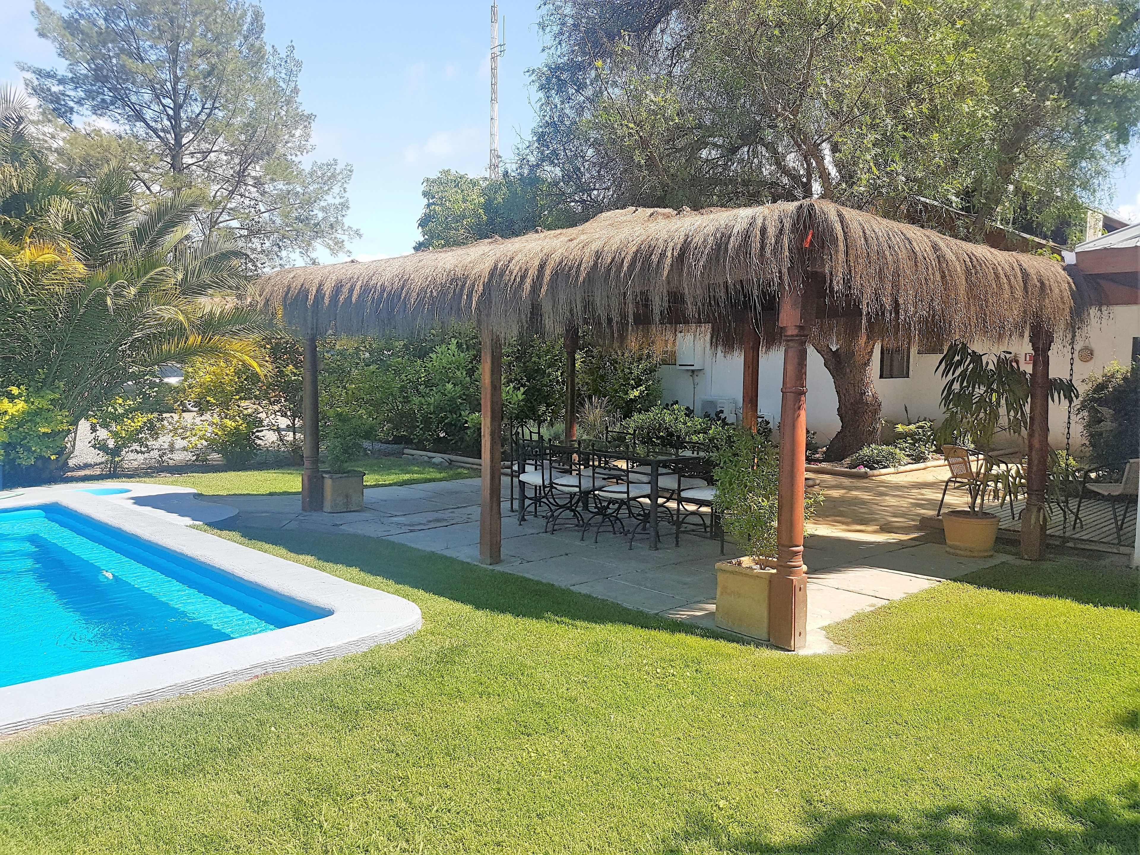 Un espace piscine agrémenté d’un gazebo à toit de chaume, de coins salon extérieurs et d’une pelouse bien entretenue.