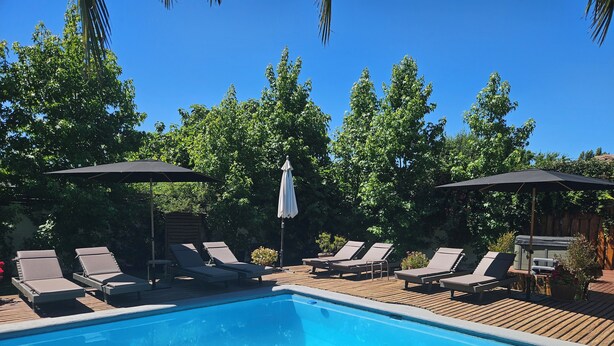Une piscine entourée d’arbres, avec des chaises longues et des parasols.