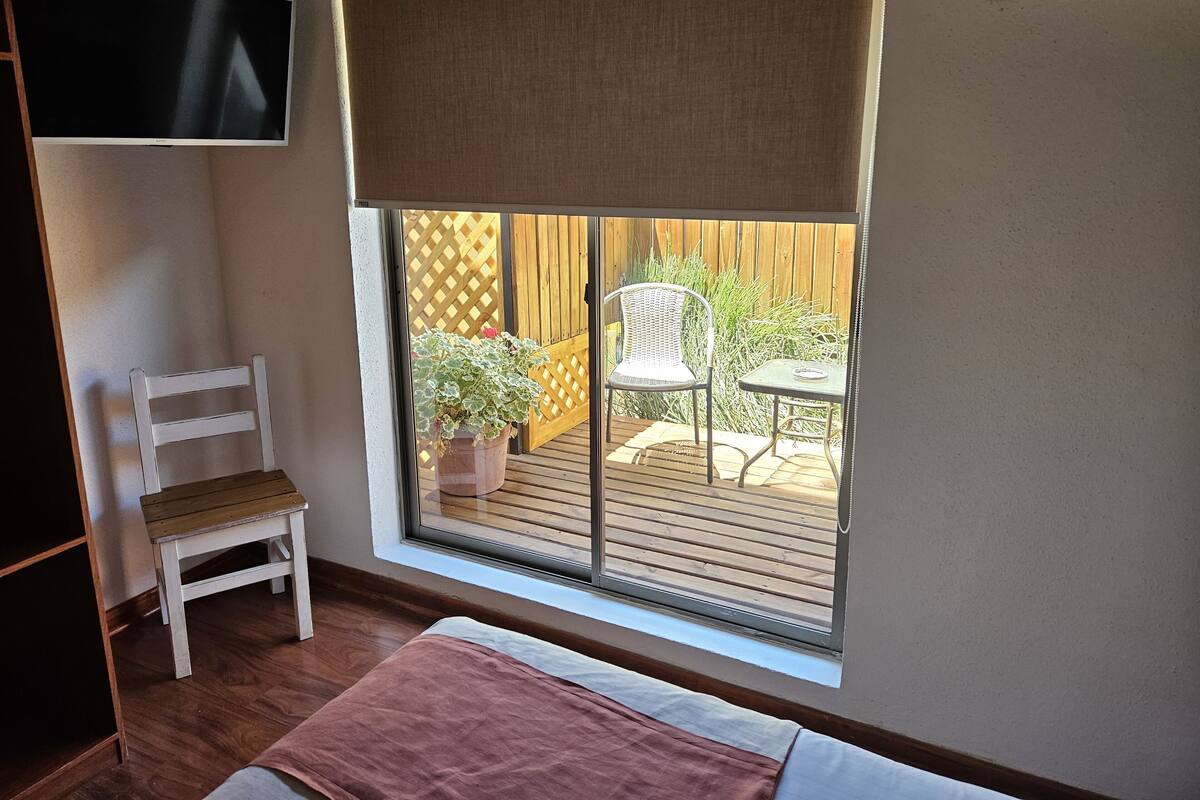 Une chambre avec un lit, un téléviseur fixé au mur, une fenêtre donnant sur un patio et un fauteuil.