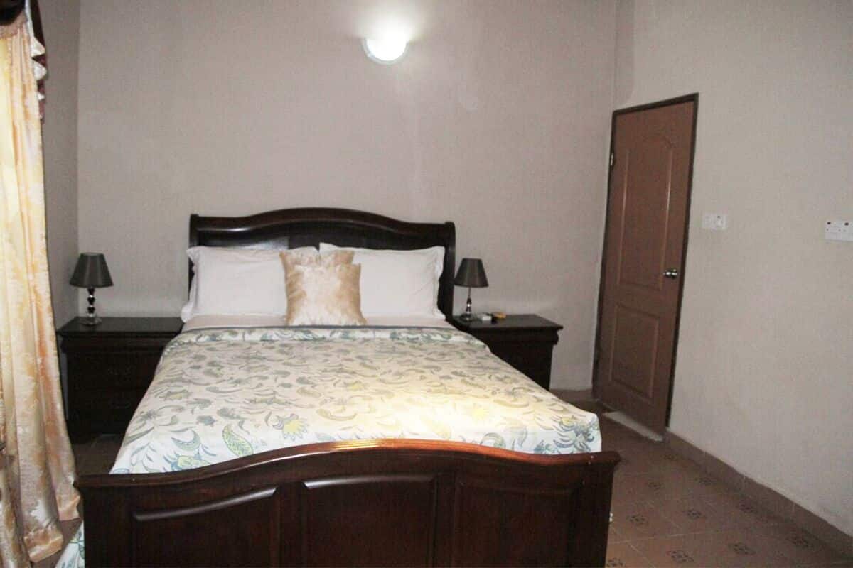 Una cama bien hecha con una colcha estampada con motivos florales, dos mesitas de noche con lámparas y una puerta cerrada.