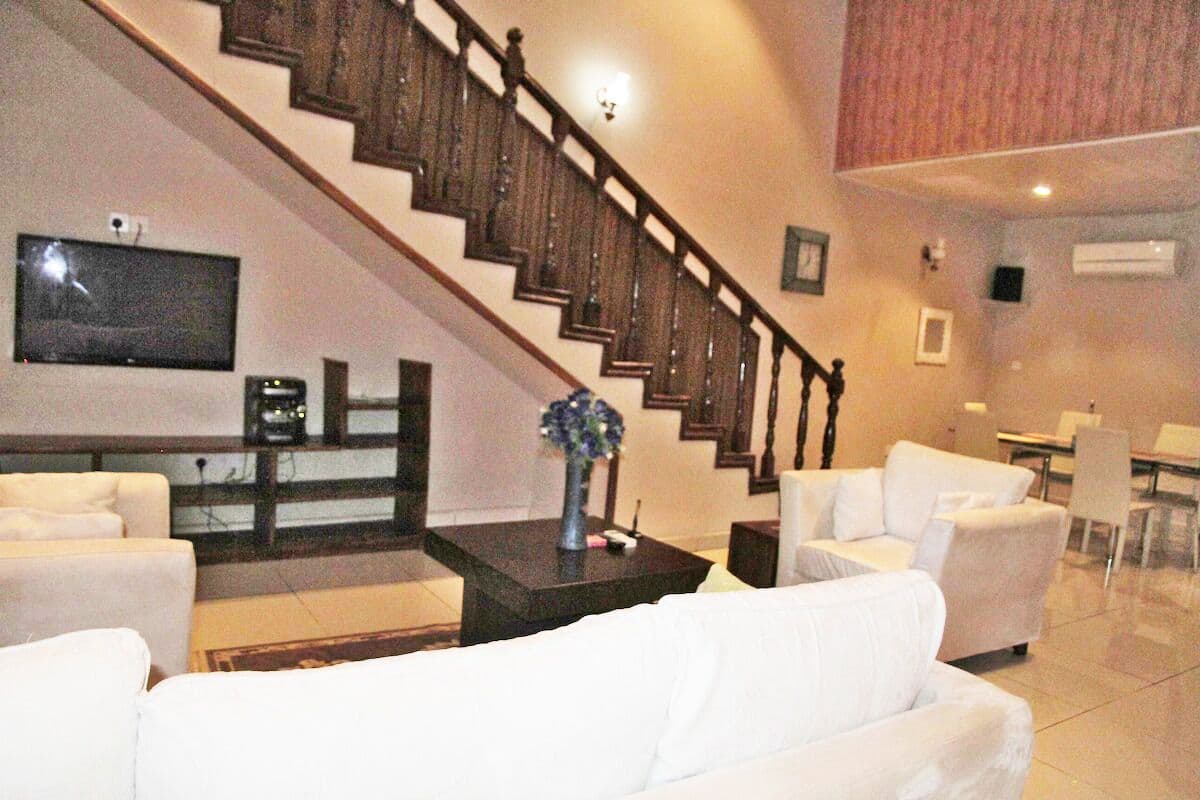 Una sala de estar con una escalera, sofás blancos, una mesa de centro y un televisor de pantalla plana.