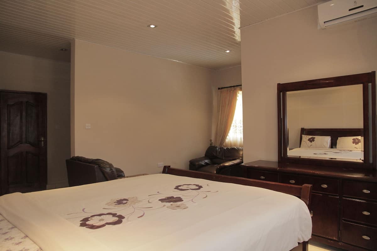 Una habitación de hotel con una cama, un tocador de madera, un espejo y una ventana con cortinas.