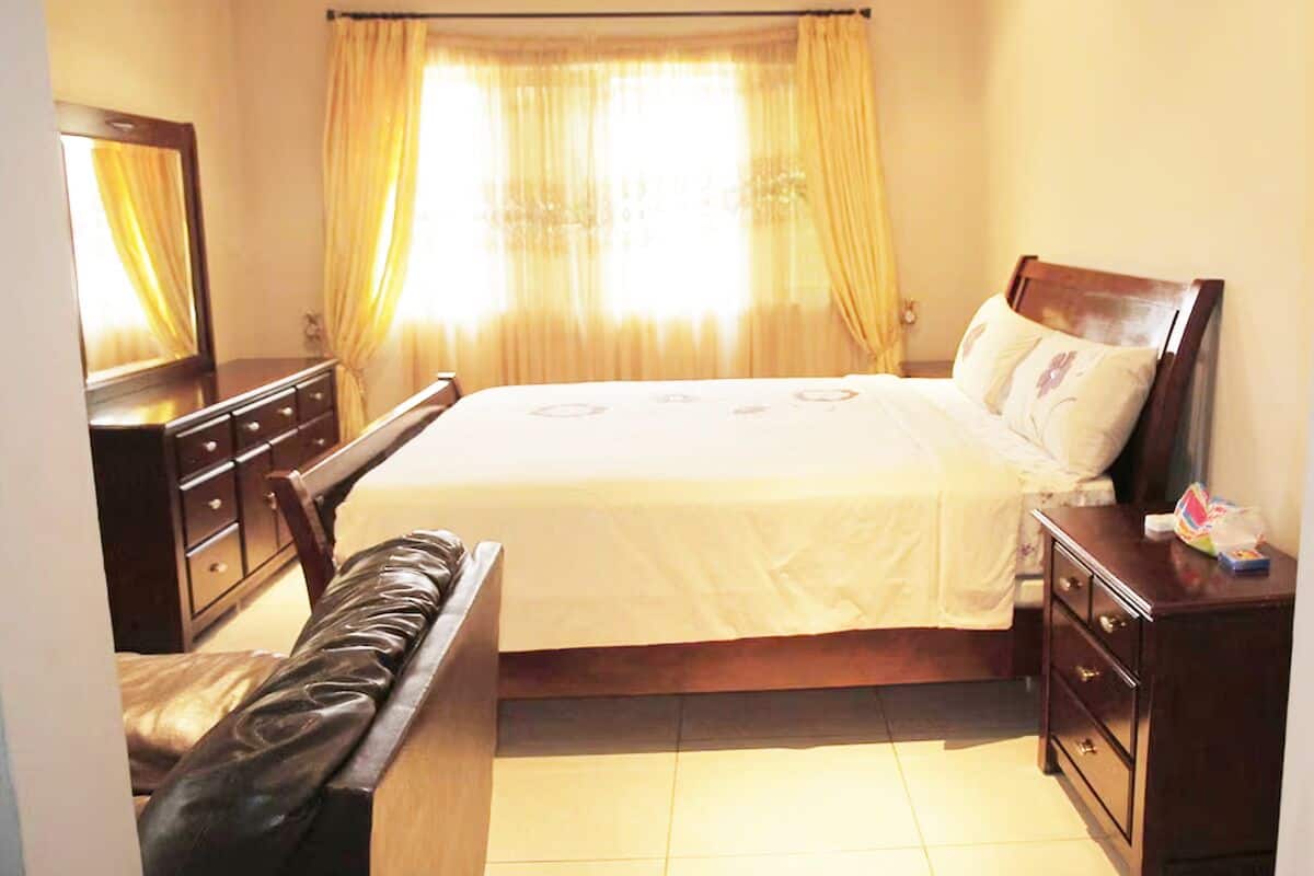 Un dormitorio con cama, cómoda de madera, banco y espejo.
