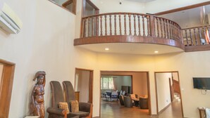 A spacious living area with a high ceiling, a wooden staircase, and a view of the dining area. - Occasions (Freetown)