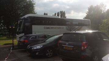 Een parkeerplaats met een touringcar met de aanduiding "COACHPARTNERS" en verschillende auto's.