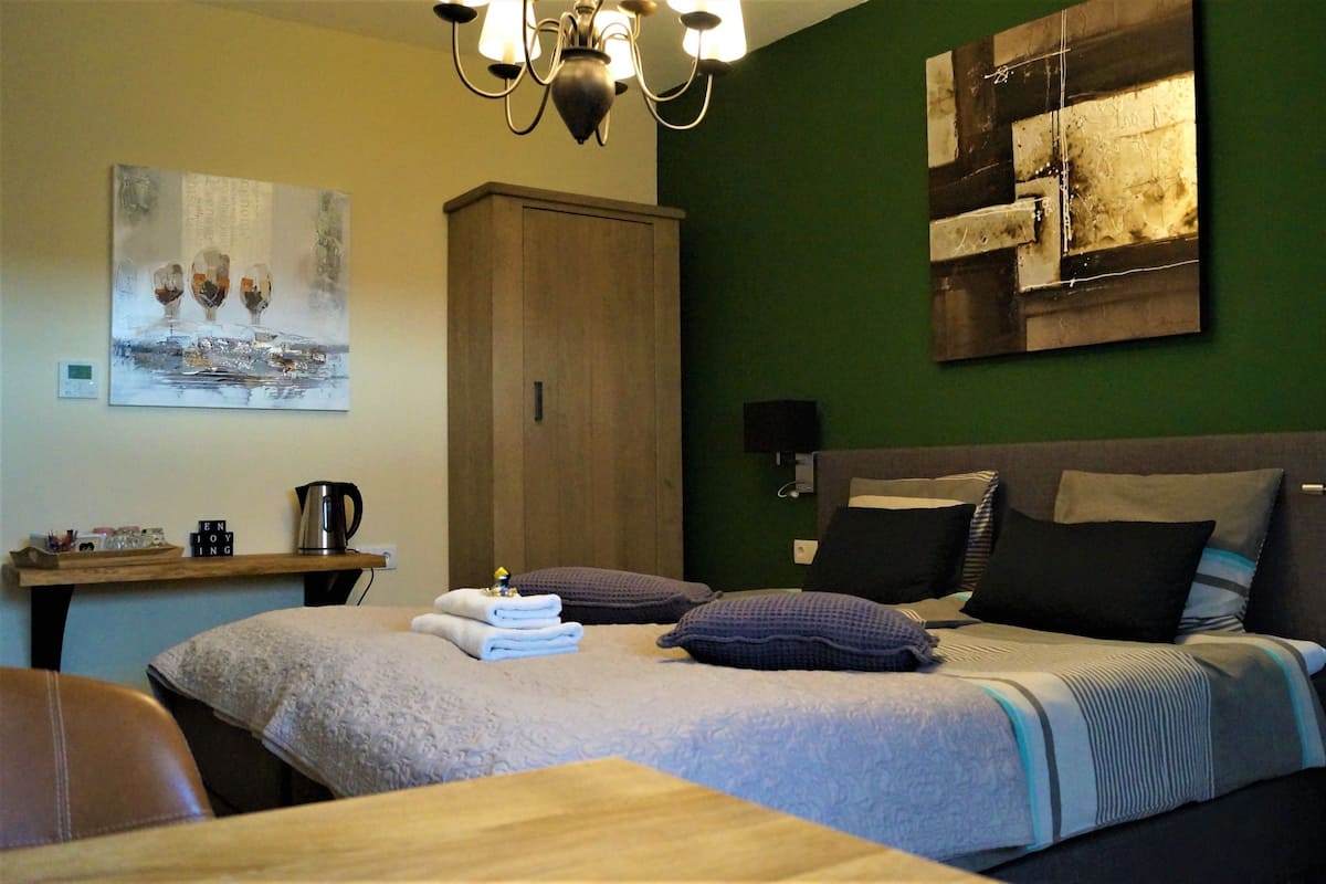Un dormitorio ordenado con cama, almohadas, una mesita de noche, un escritorio y un cuadro en la pared.