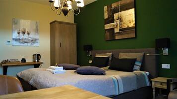 Un dormitorio ordenado con cama, almohadas, una mesita de noche, un escritorio y un cuadro en la pared.