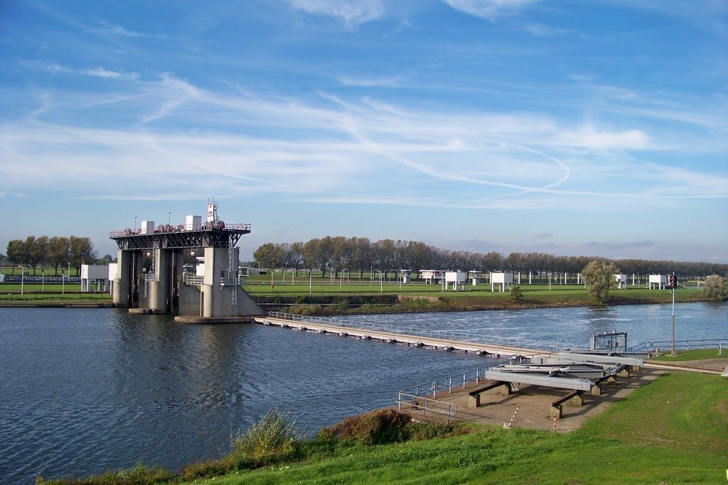 Ein Schlosssystem mit Brücke über einem Fluss, umgeben von Grünflächen und blauem Himmel.