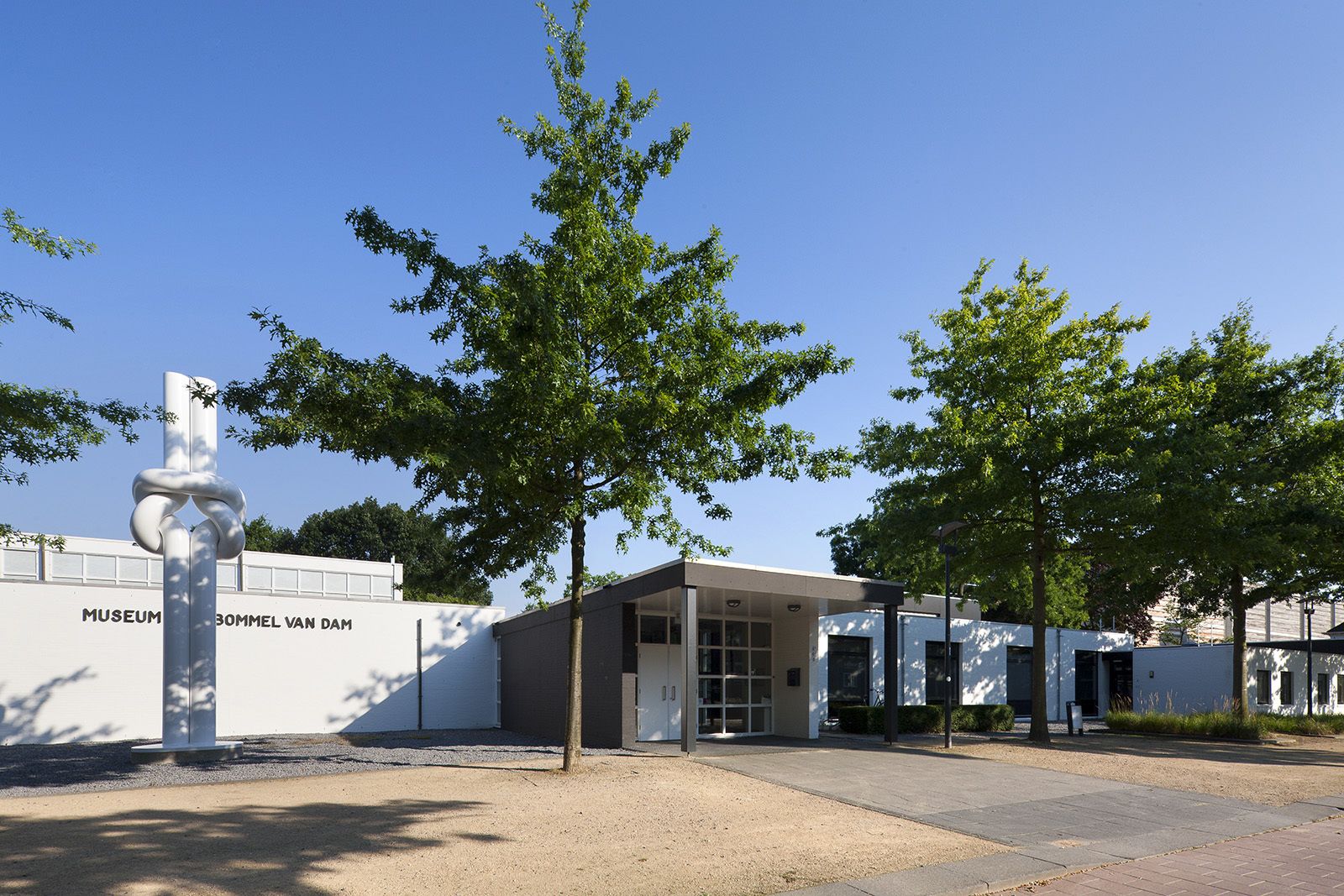 A museum entrance with a modern building, a sculpture, and trees.