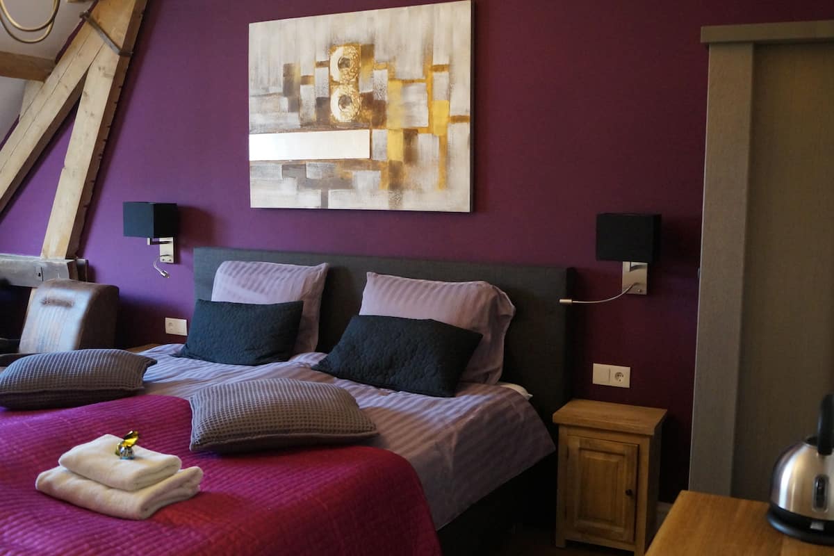 Una habitación de hotel con cama, un cuadro en la pared, un escritorio con hervidor y un mueble de madera.