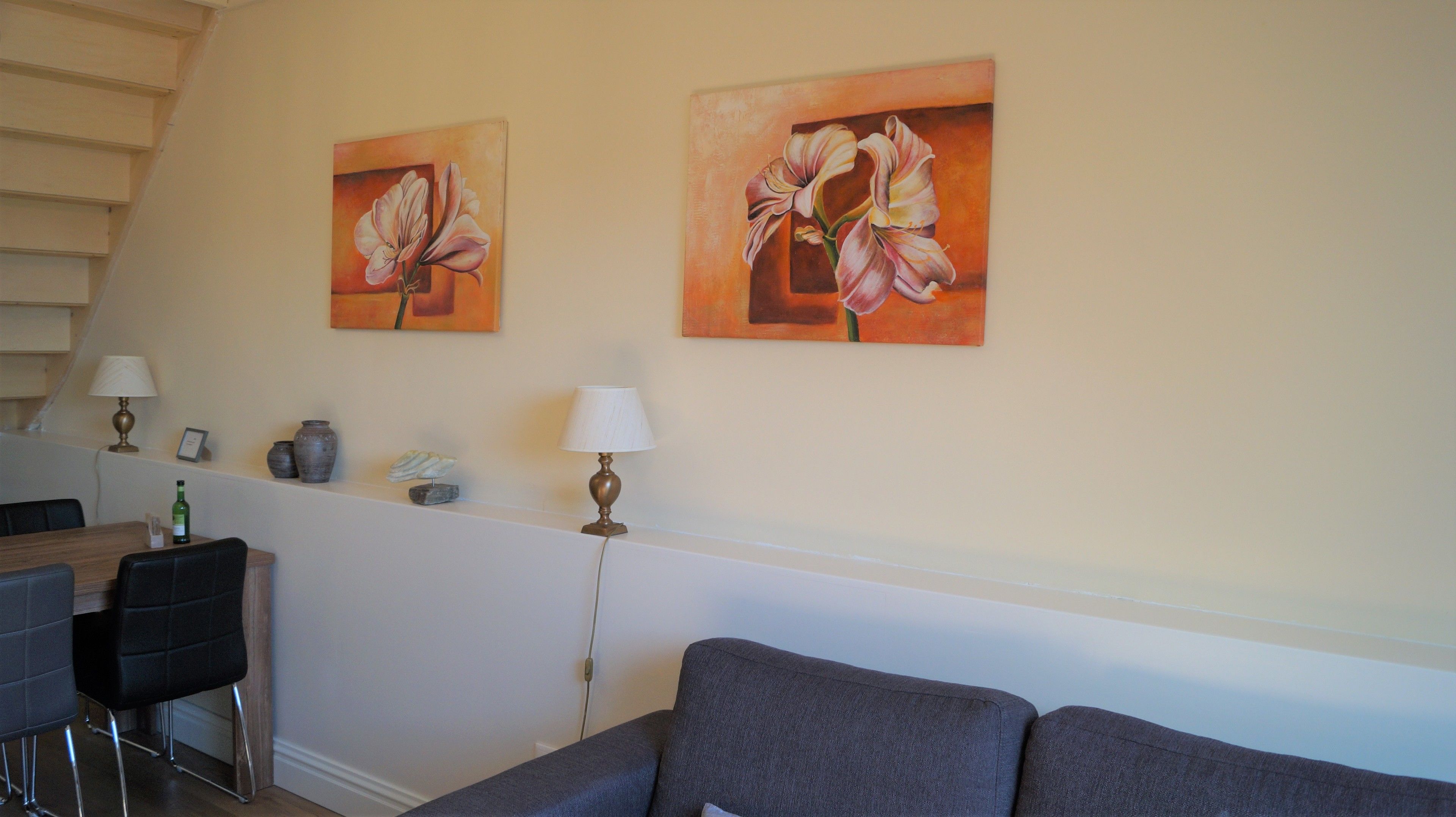 A living room with a sofa, two paintings of flowers, a lamp, a vase, and a bottle on a table.