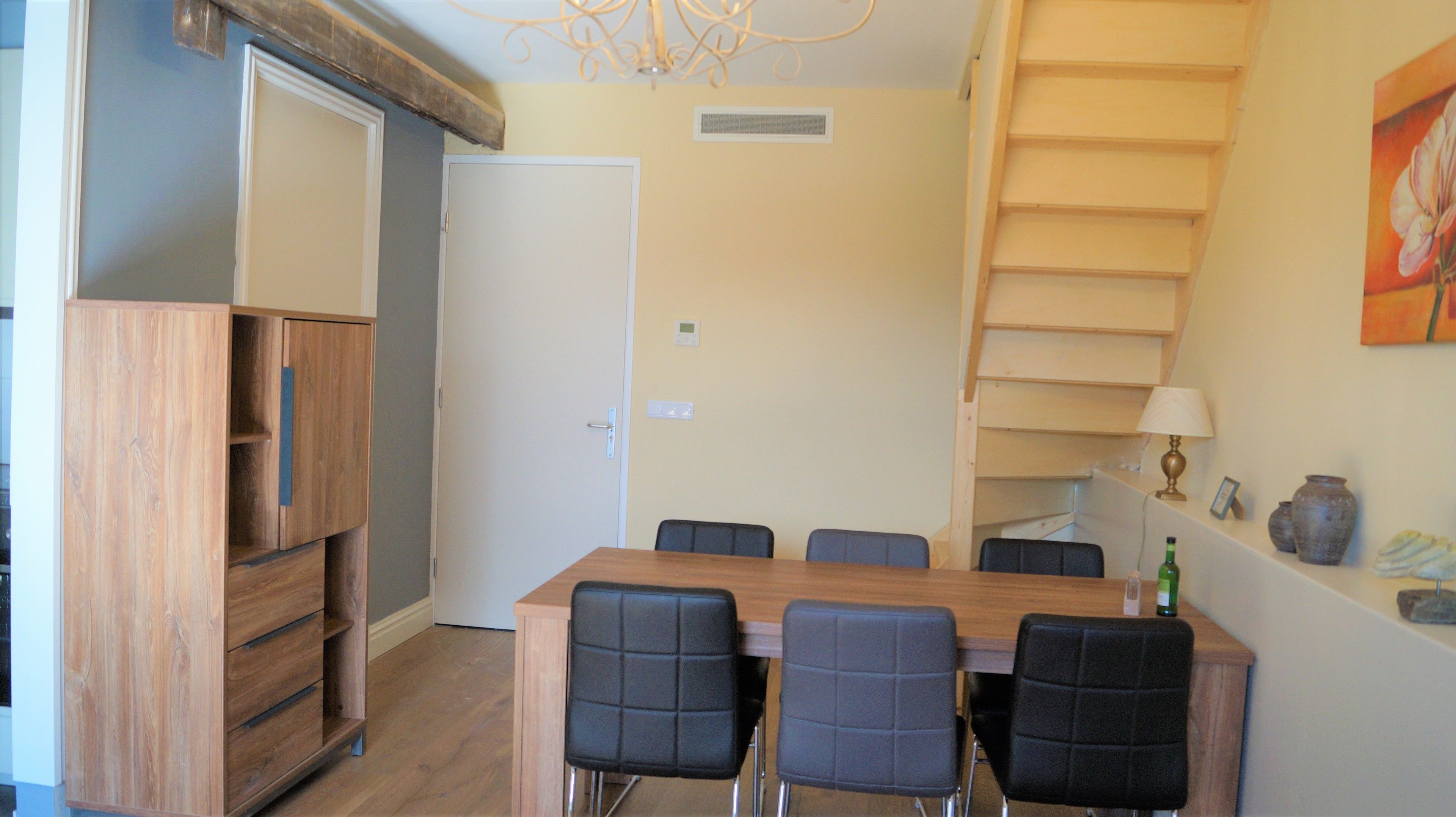 A dining area with a wooden table and six chairs, a wooden cabinet, and a staircase with a railing.