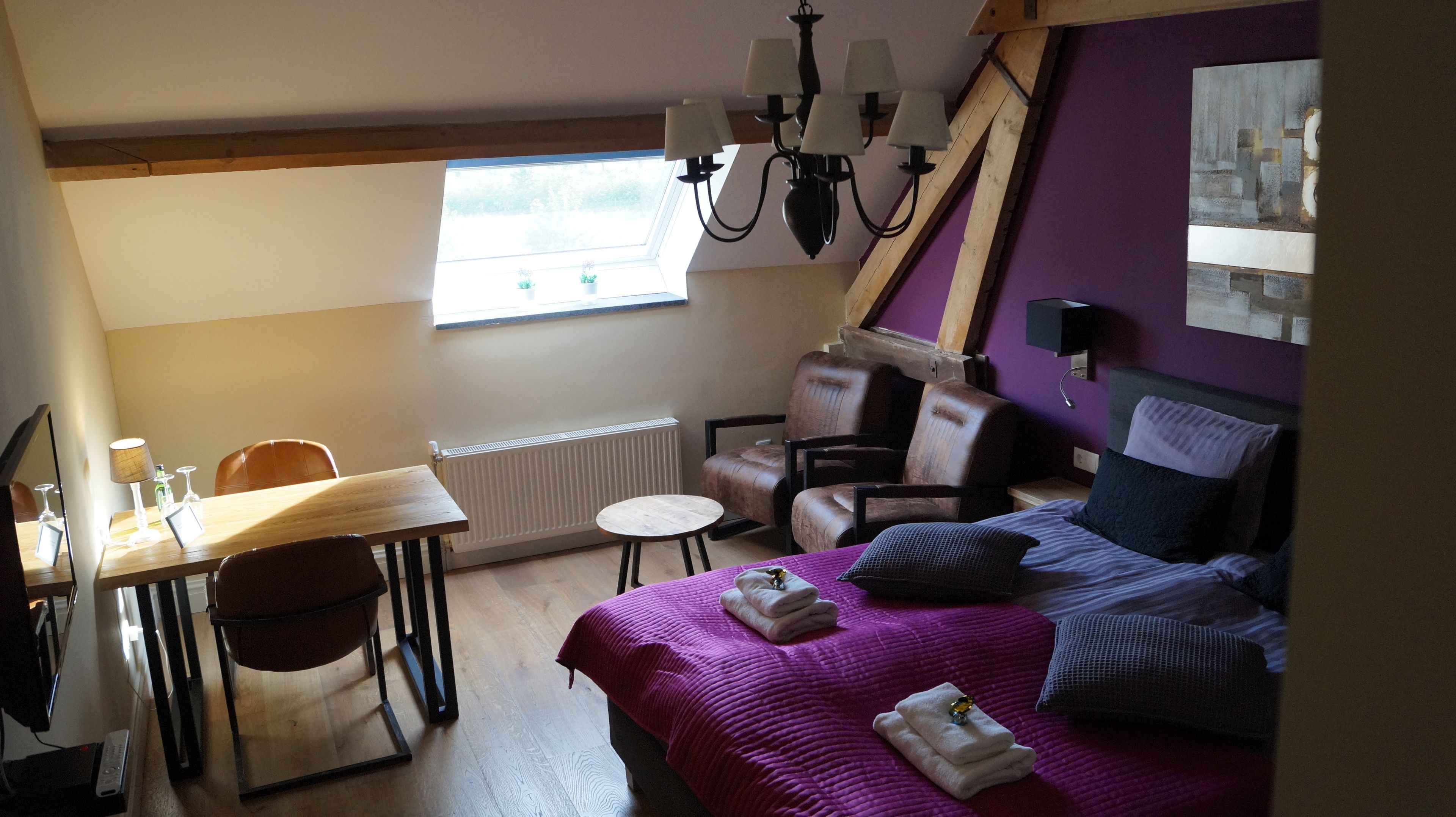 Una habitación con cama, silla, mesa, radiador y ventana.