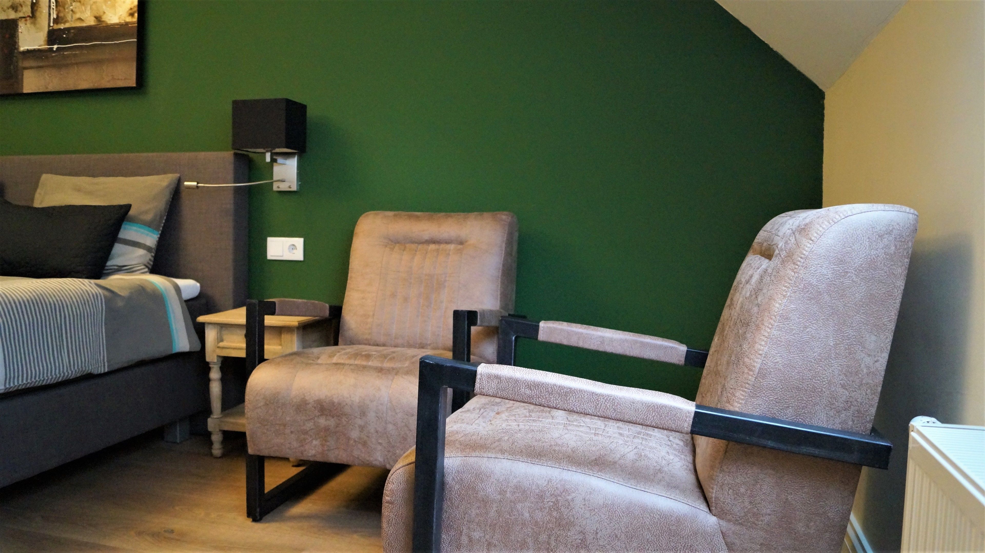 A room with a bed, two armchairs, a small table, and a wall-mounted speaker.