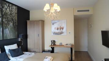 Un dormitorio con cama, armario, escritorio con hervidor, un cuadro y televisor.