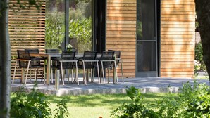 Une maison moderne dotée d’un coin repas comprenant une table et des chaises, de grandes fenêtres et une vue sur le jardin.