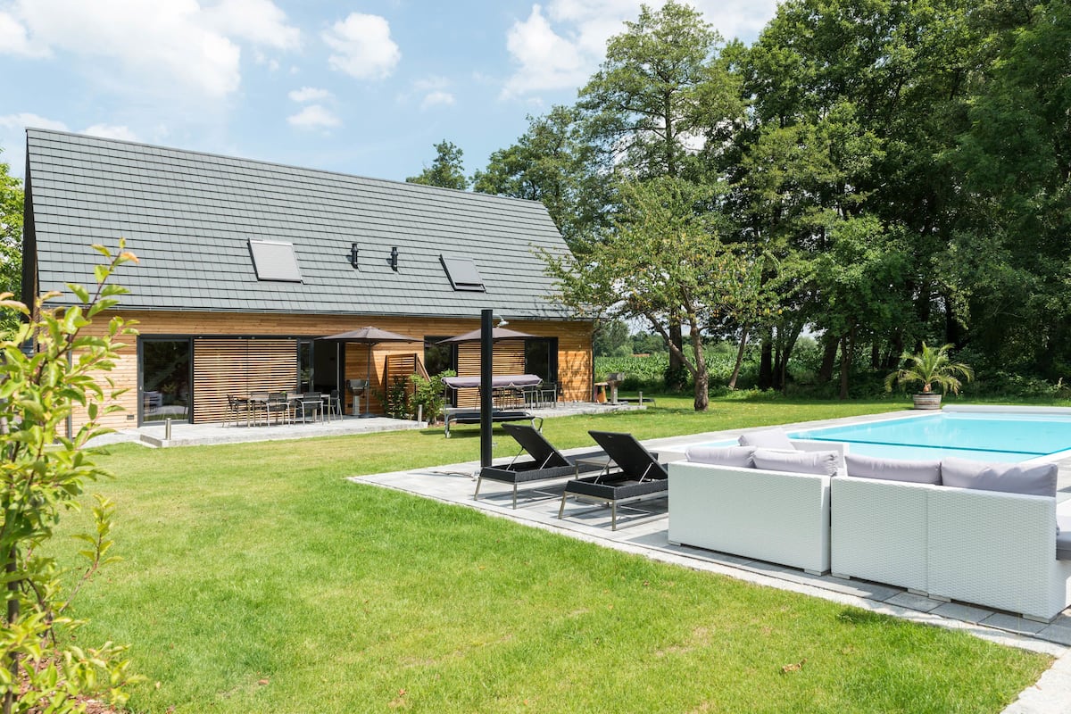 A modern house with a swimming pool, outdoor seating, and a well-maintained lawn.