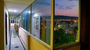 A corridor with glass walls and a view of a cityscape at dusk. - Royal Palm - Hotel Near Udaipur Railway Station (Udaipur)