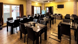 A conference room with multiple tables and chairs, a flat-screen TV mounted on the wall, and a window with curtains. - Royal Palm - Hotel Near Udaipur Railway Station (Udaipur)