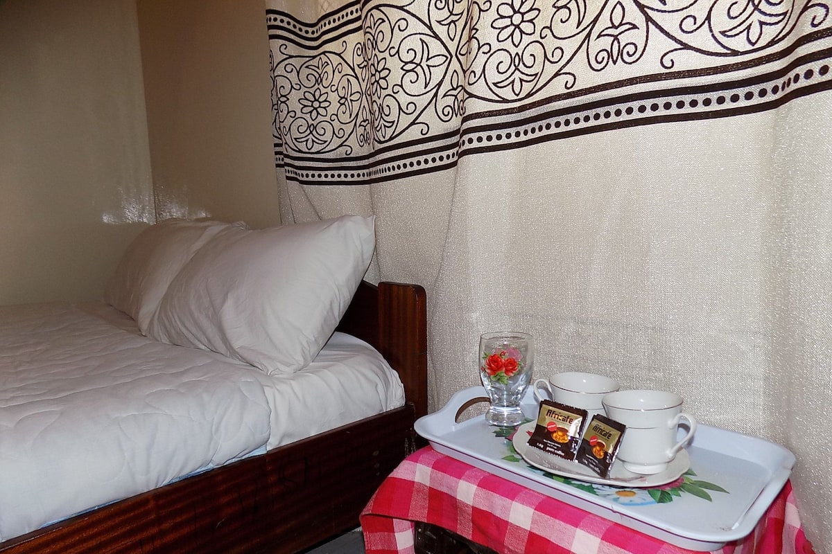 A neatly made bed with white bedding, a wooden headboard, and a decorative curtain with a black and white pattern.