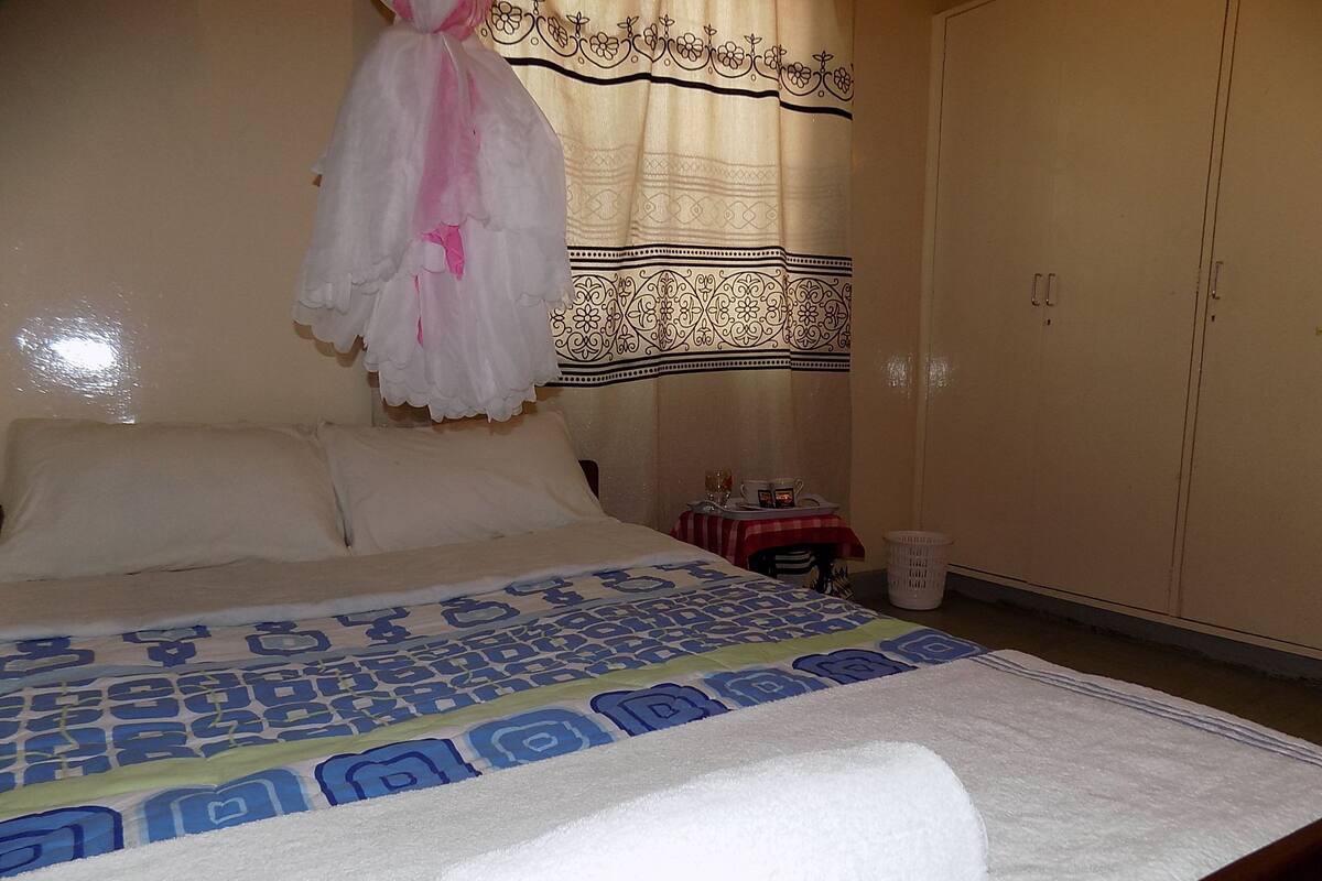 A bedroom with a bed, a mosquito net, a table with a tray, and a wardrobe.