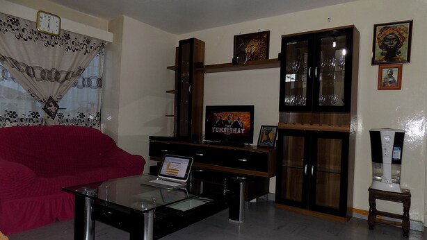 Un salón con un sofá rojo, una mesa de centro de vidrio, un televisor sobre un mueble de madera y un aparador con puertas de cristal.