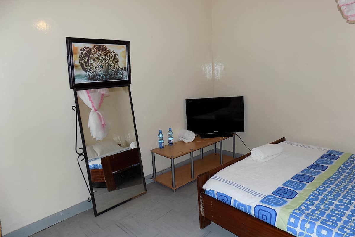 A hotel room with a bed, a television, a mirror, and a small table with two bottles of water.