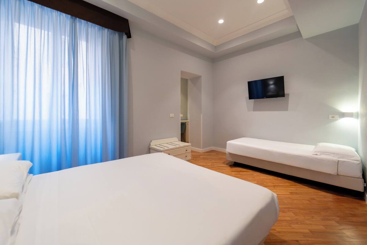 A hotel room with a large bed, a smaller bed, a TV mounted on the wall, and a wooden floor.