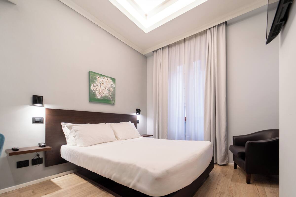A modern hotel room with a large bed, a desk, a chair, and a painting on the wall.